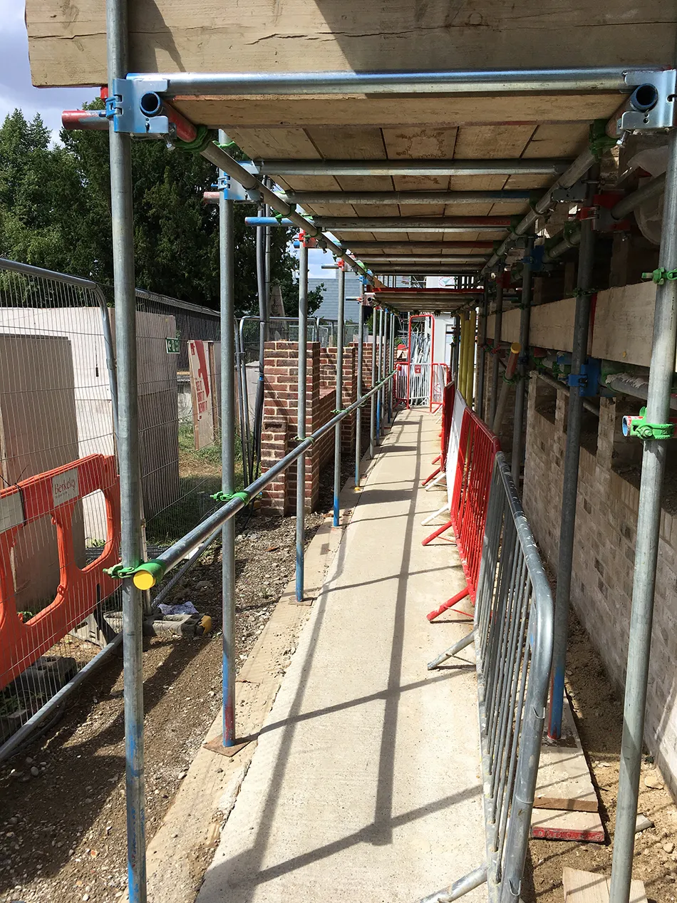 Temporary works scaffold covered walkway alongside a building under construction